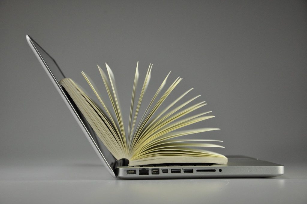 Stockfoto: Laptop mit aufgeschlagenem Buch darauf zu sehen 